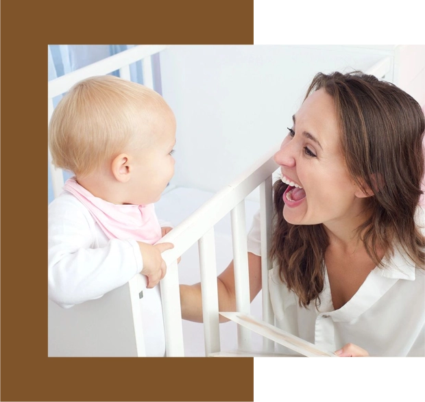 A woman and baby in a crib laughing.