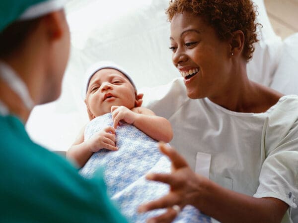 A woman holding a baby while another person looks on.