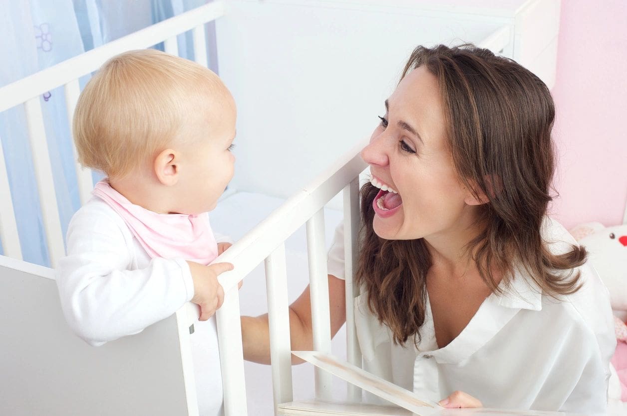 A woman is playing with her baby in the crib